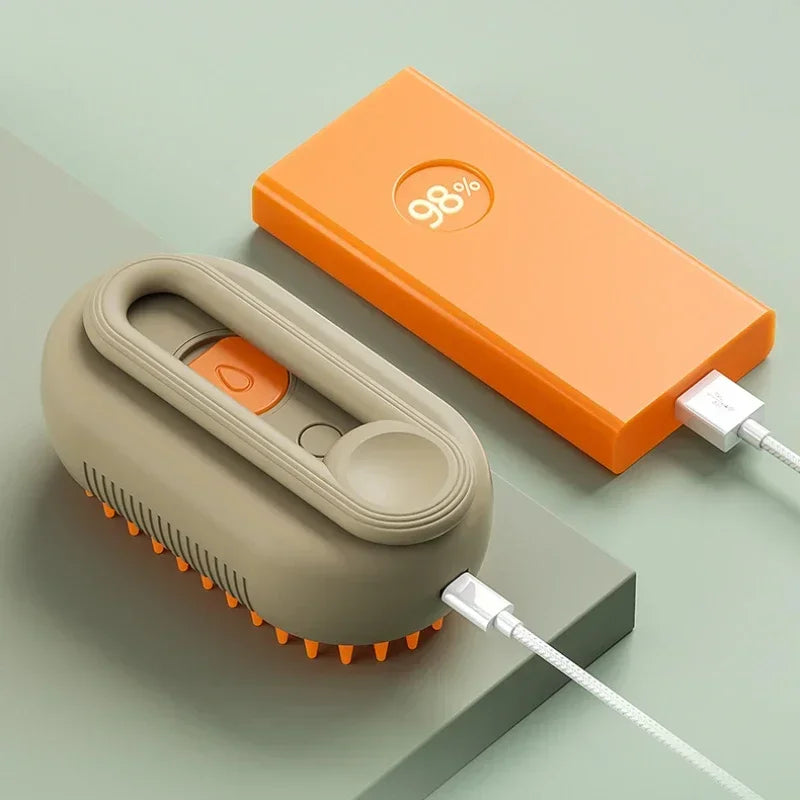 Taupe electric grooming brush with orange bristles being charged by an orange power bank on a green surface.