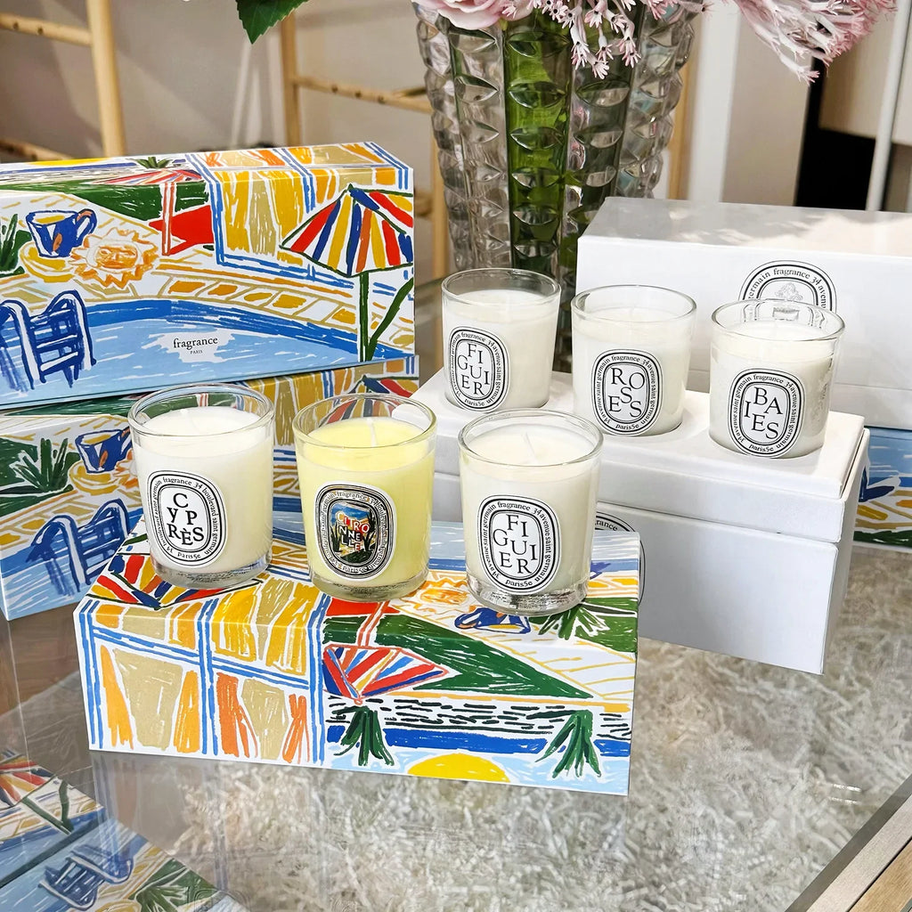 Set of scented candles in clear glass jars with white and yellow wax, displayed on decorative illustrated gift boxes.