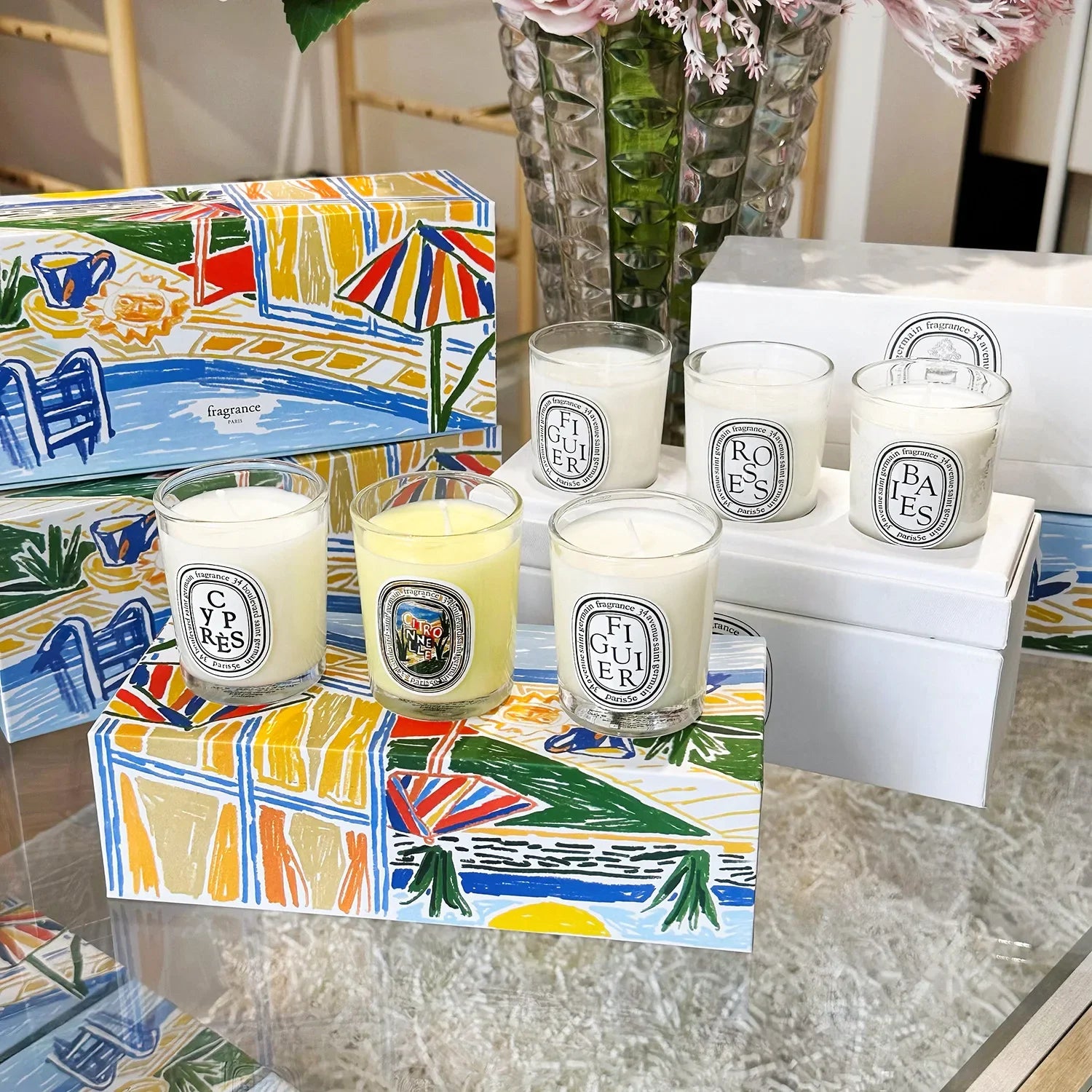 Set of scented candles in clear glass jars with white and yellow wax, displayed on decorative illustrated gift boxes.