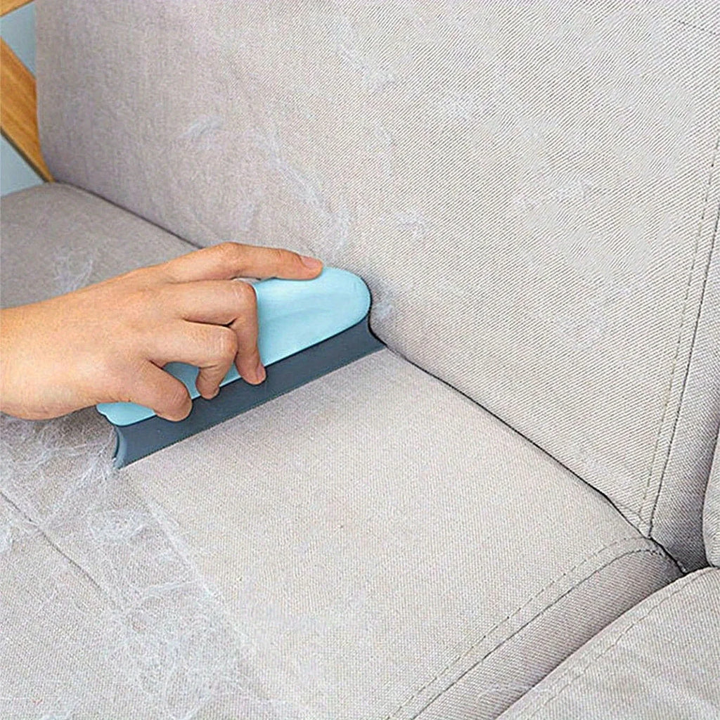 A hand using a light blue and grey lint remover tool to clean pet hair from a beige fabric sofa.