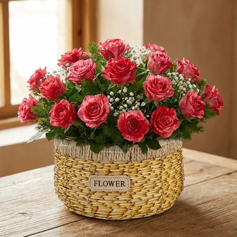 A bouquet of variegated pink roses in a round, woven basket with a "FLOWER" label, sitting on a wooden table.