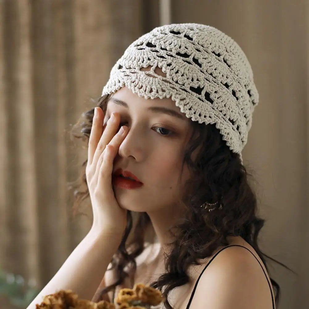 A woman wearing an off-white, vintage-style crochet beanie featuring an intricate, hollow lace pattern.