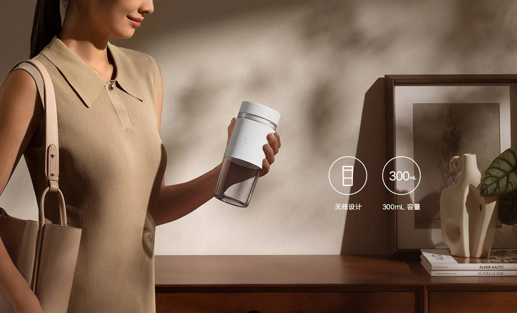 A woman holds a portable, minimalist white 300ml blender with a clear base against a warm, neutral background.