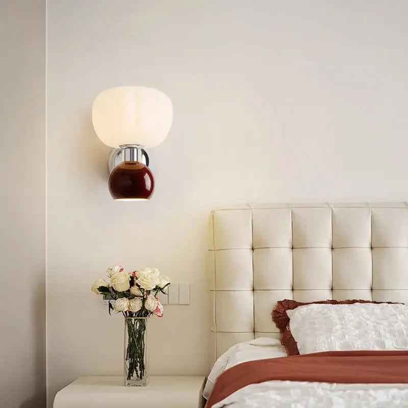 Modern cream-style wall lamp with a spherical white glass shade and a polished dark red base, mounted in a bedroom.