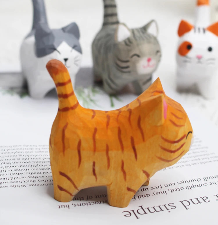 Hand-carved wooden cat figurines in various colours and patterns, featuring minimalist, rustic designs.