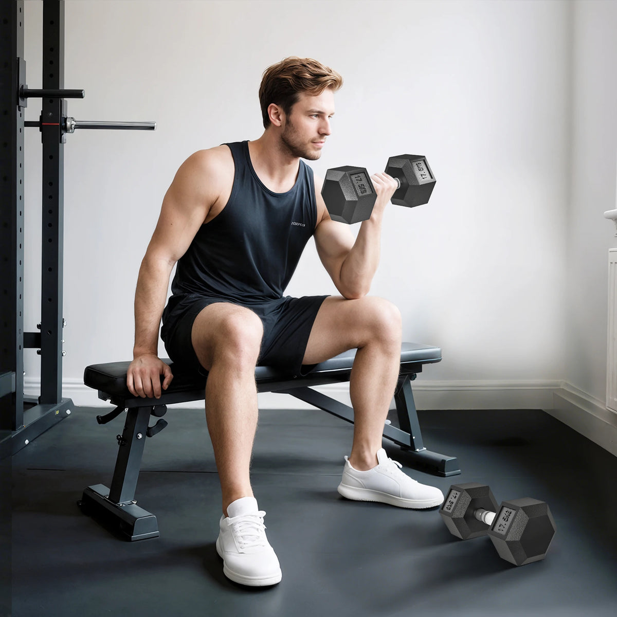 Man sitting on a bench lifts a black rubber 17.5kg hex dumbbell, with a matching one on the floor.