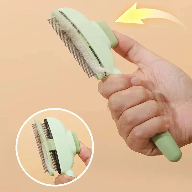 A hand holds a sage green self-cleaning pet grooming brush with fine metal bristles, showing hair being removed.
