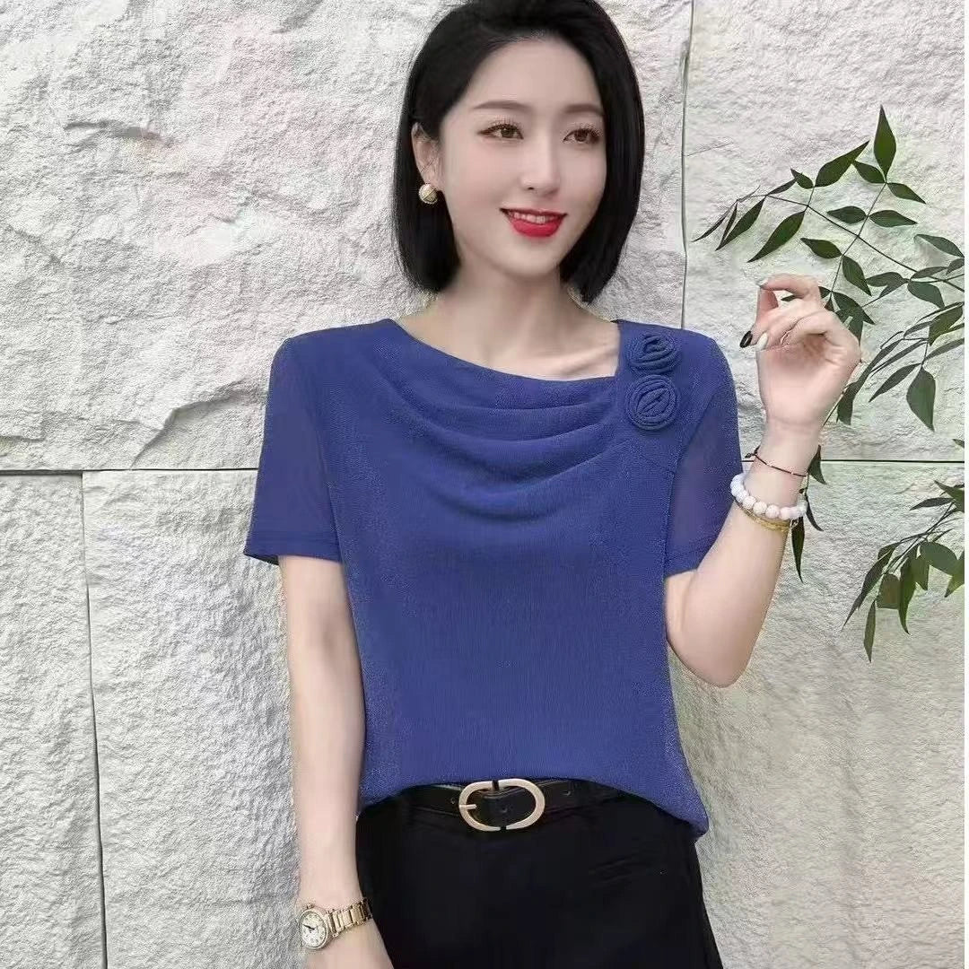 Blue short-sleeved blouse with a cowl neckline, rosette detail, and sheer sleeves, paired with black trousers.