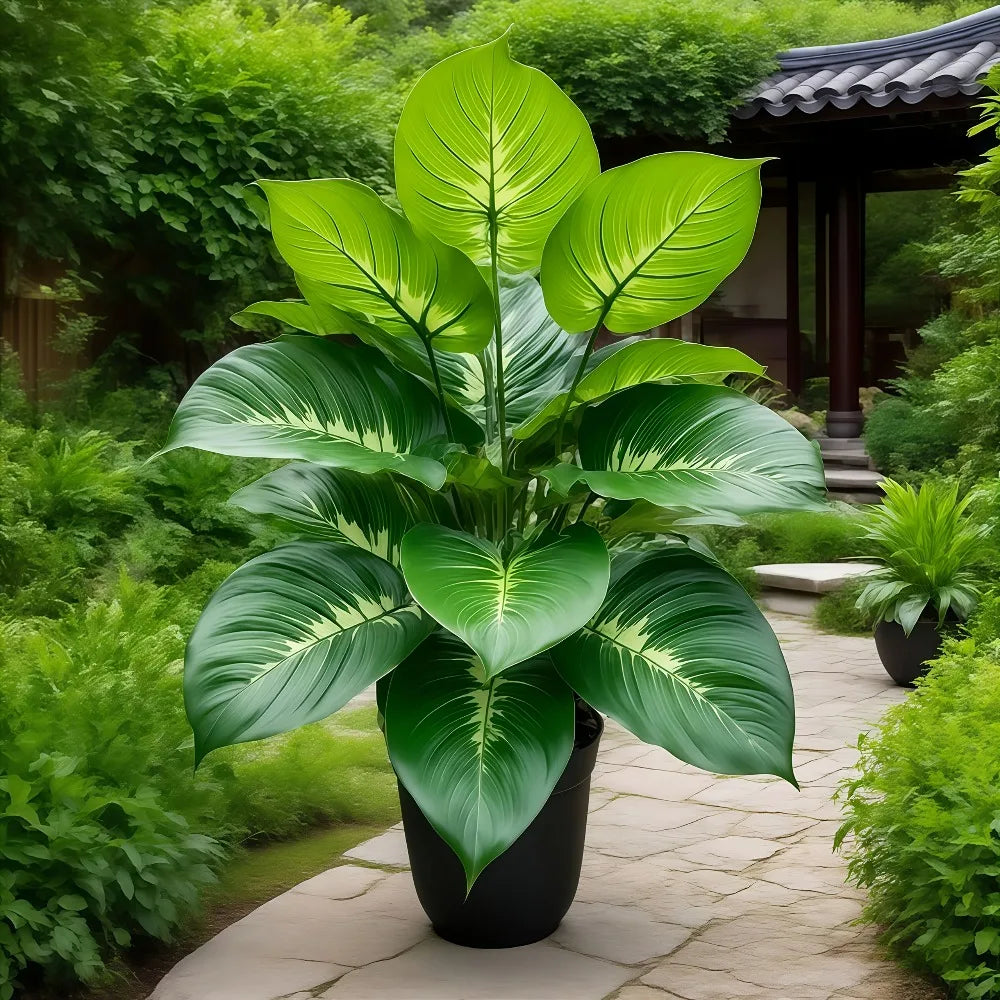 Large artificial plant in a black pot with broad, variegated green leaves, set on a stone garden path.