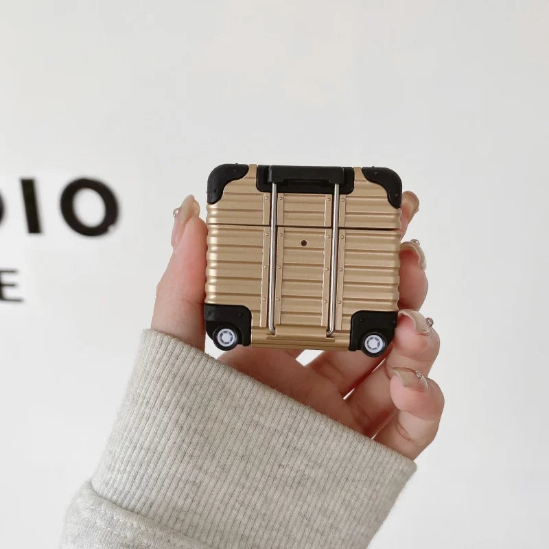 Gold metallic suitcase-style AirPods case with black corner detailing, held in a hand.