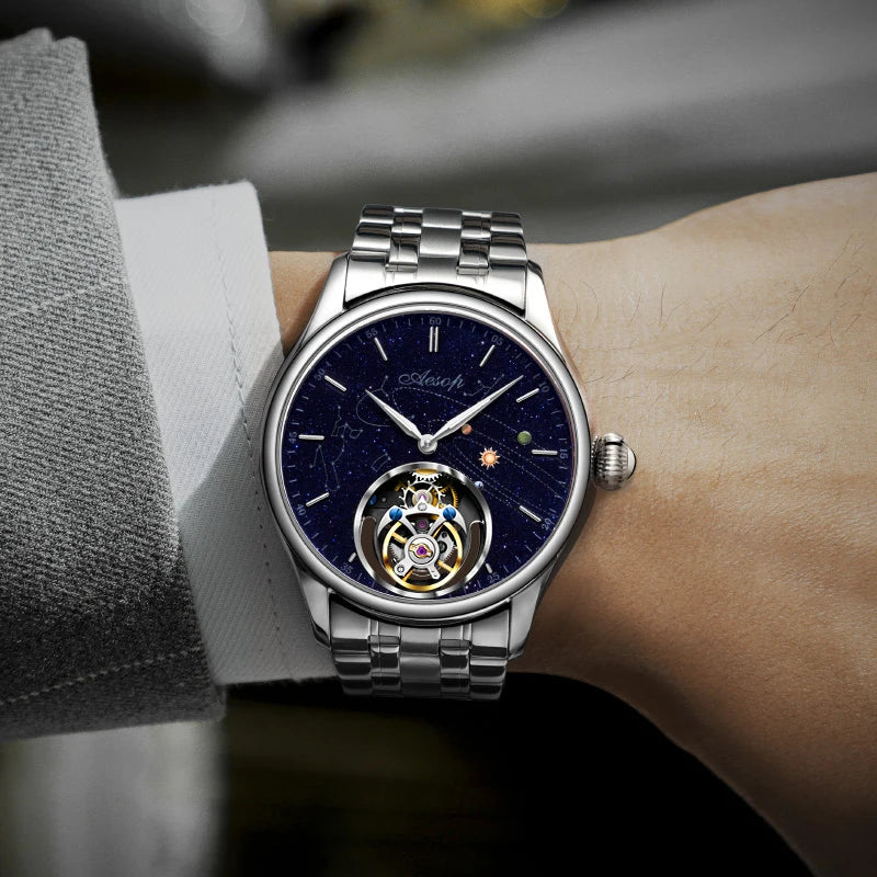 AESOP silver mechanical watch with round case, blue starry dial, visible tourbillon, and metal bracelet on wrist.
