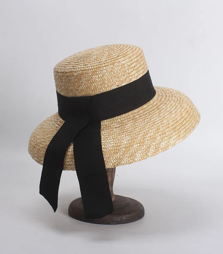 Elegant wide-brim straw sun hat in natural beige, featuring a black ribbon band with dangling tails.