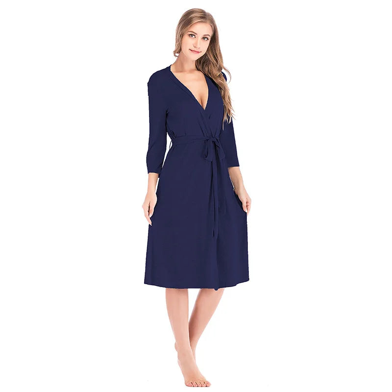 A woman wearing a knee-length, navy blue wrap robe with three-quarter sleeves and a matching tie-waist belt.