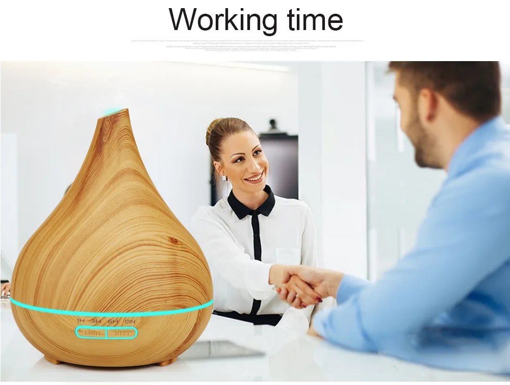 Teardrop-shaped wooden essential oil diffuser with glowing blue light rings, on a desk during a professional handshake.