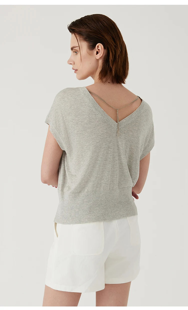 Light grey knit top with a deep V-back featuring delicate chain detail, worn with white shorts.