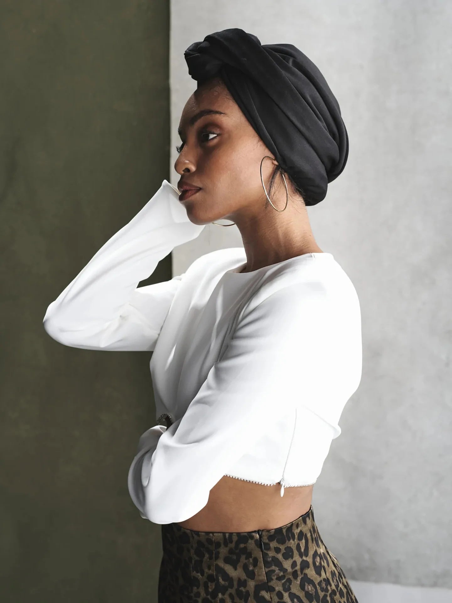 A woman wearing a black vintage-style knotted turban hat, paired with a white long-sleeved crop top.