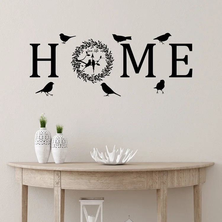 Black self-adhesive wall sticker featuring the word 'HOME' with a leaf wreath and bird silhouettes.
