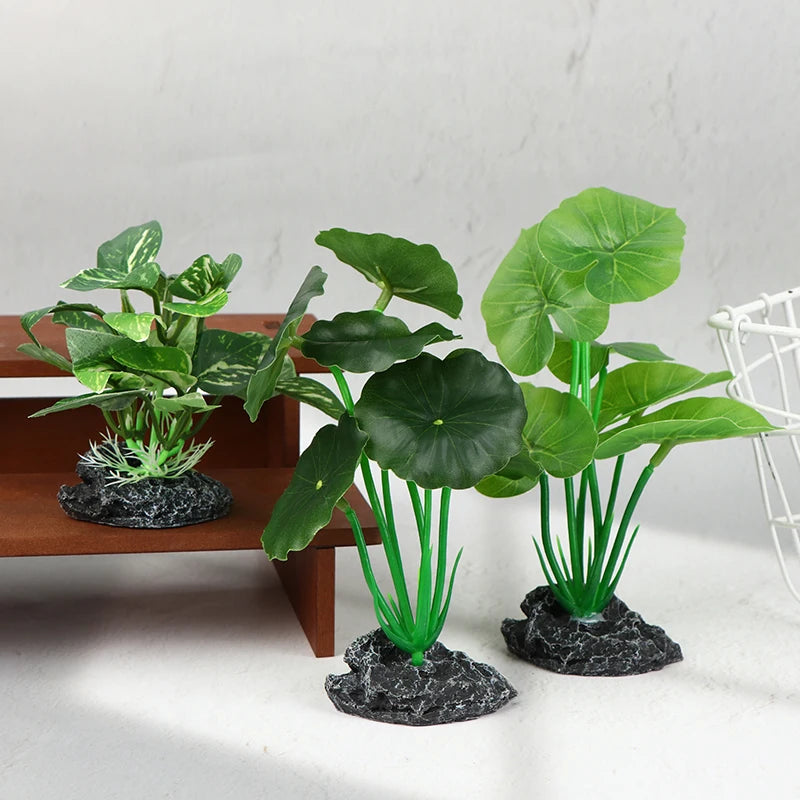 Three artificial aquarium plants with sturdy green stems and rock-textured bases stand on a white surface.