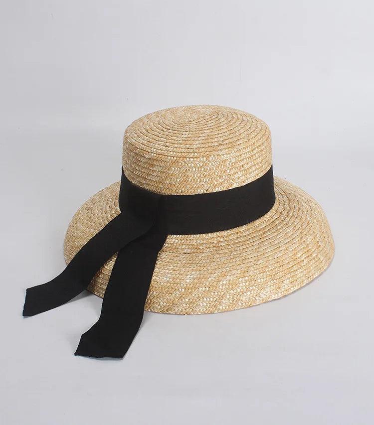 A natural-toned straw boater hat featuring a wide brim and a black ribbon band with dangling tails.