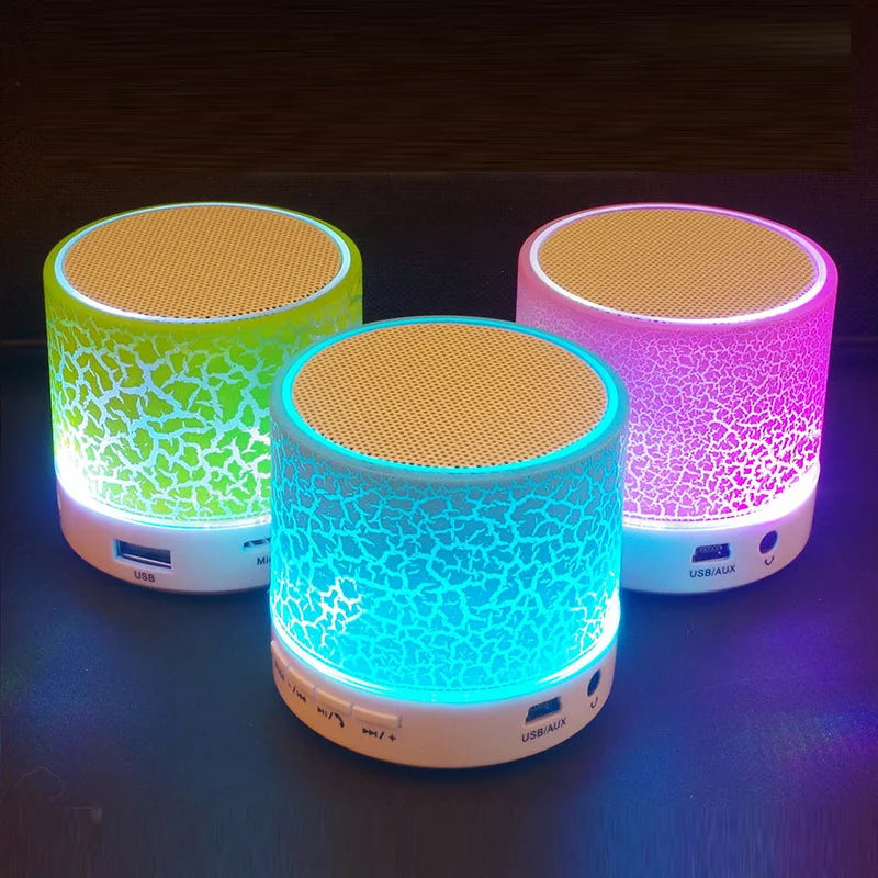 Three portable, cylindrical wireless speakers with crackle-effect LED light casings in green, blue, and pink.