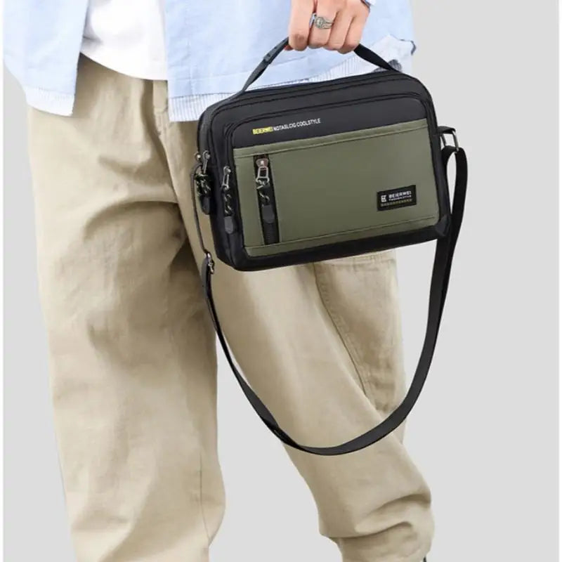 Black and olive green men's crossbody bag with a zip pocket, top handle, and adjustable shoulder strap.