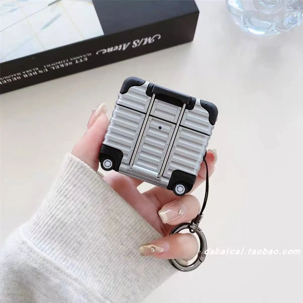 Silver suitcase-style AirPods case with a keychain, featuring a rigid, textured design and black accents.