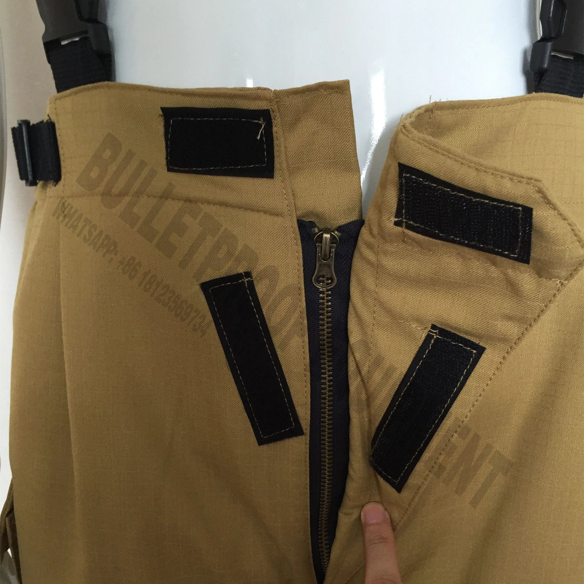 Tan tactical pants featuring a zippered fly, adjustable straps, and black hook-and-loop closures.