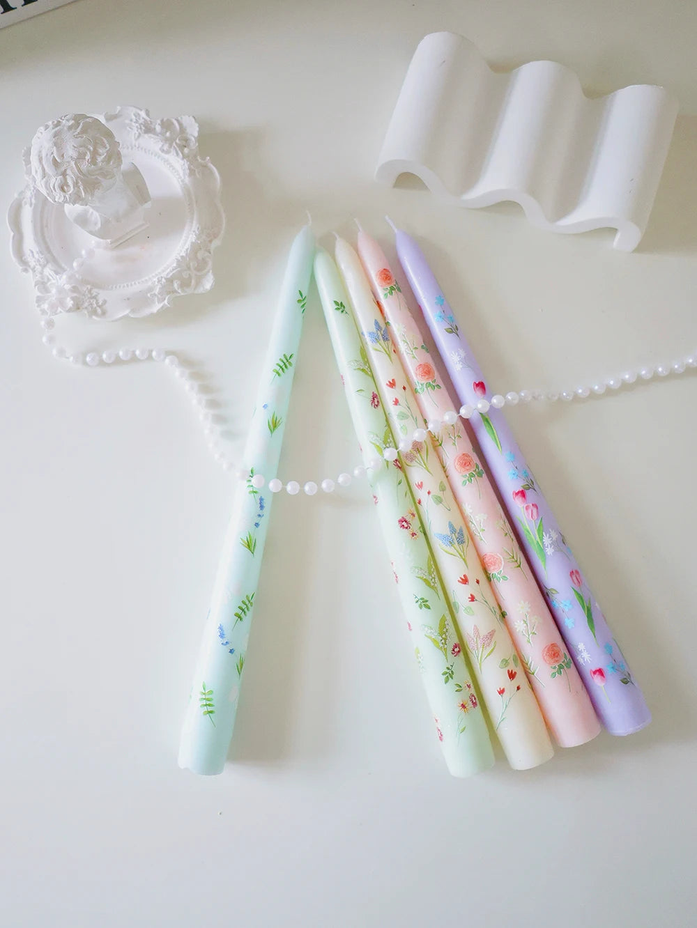 Set of five pastel taper candles featuring delicate floral and botanical prints, arranged on a white surface.