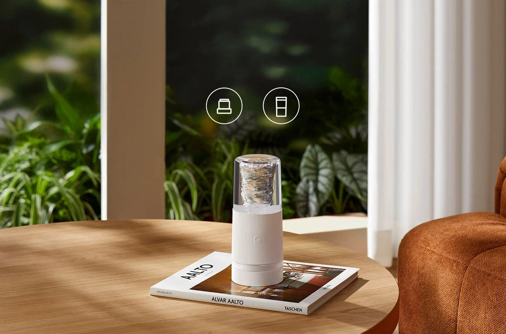 A modern, white cylindrical portable blender with a clear top sitting on a coffee table.