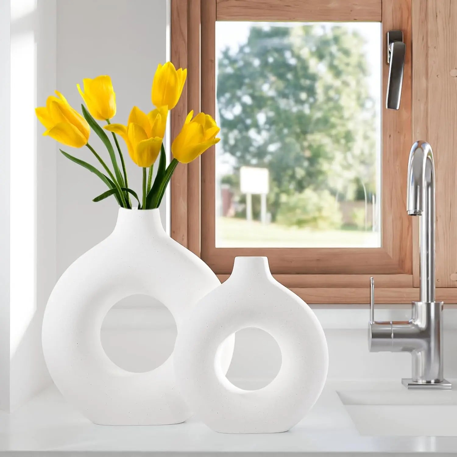 Two matte white, circular Nordic-style vases on a kitchen counter, with the larger one holding yellow tulips.