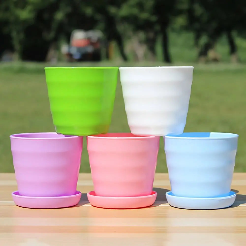 Five colorful, ribbed plastic flower pots with matching saucers stacked on a wooden table outdoors.
