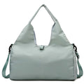 Light sage green duffel bag with dual top handles and an adjustable shoulder strap on a white background.