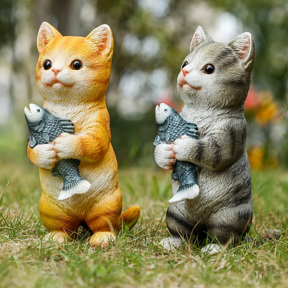 Two charming resin garden statues of an orange tabby and a grey tabby cat, each standing and holding a silver fish.