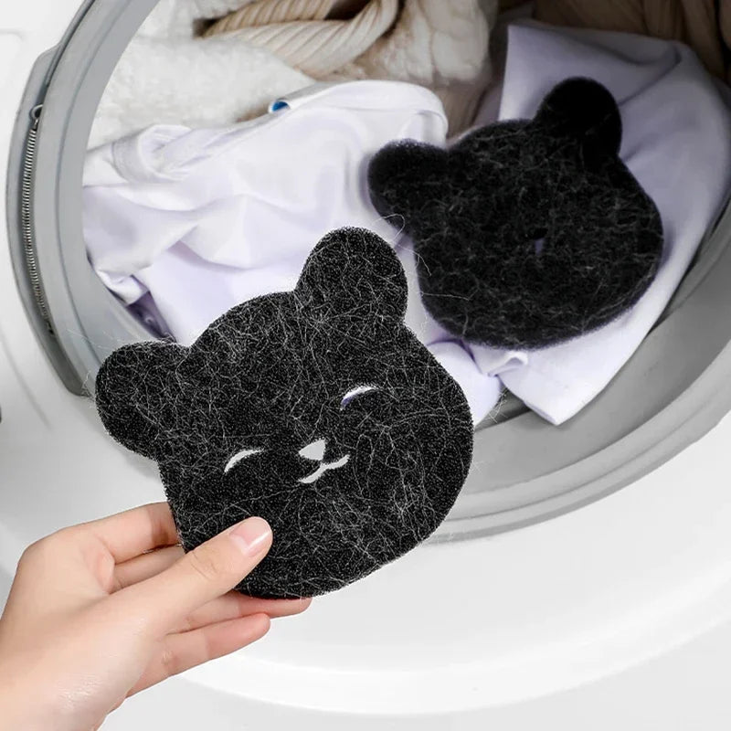 Hand holding a black bear-shaped pet hair remover sponge, with another inside a washing machine with laundry.