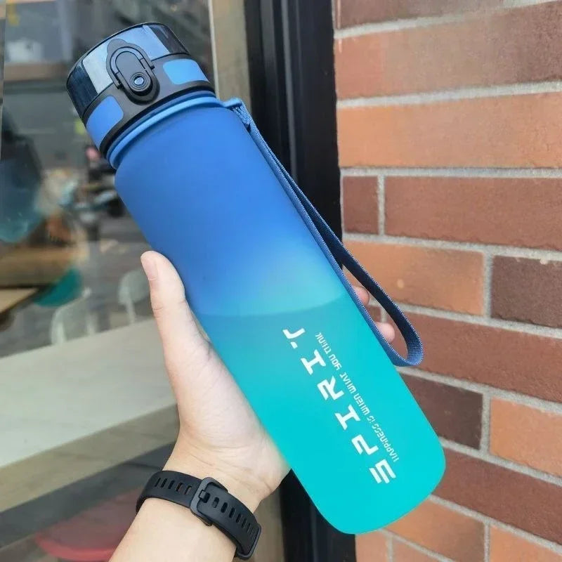 A person holds a blue ombre sports water bottle with a locking lid, carry strap, and white "SPIRIT" branding.