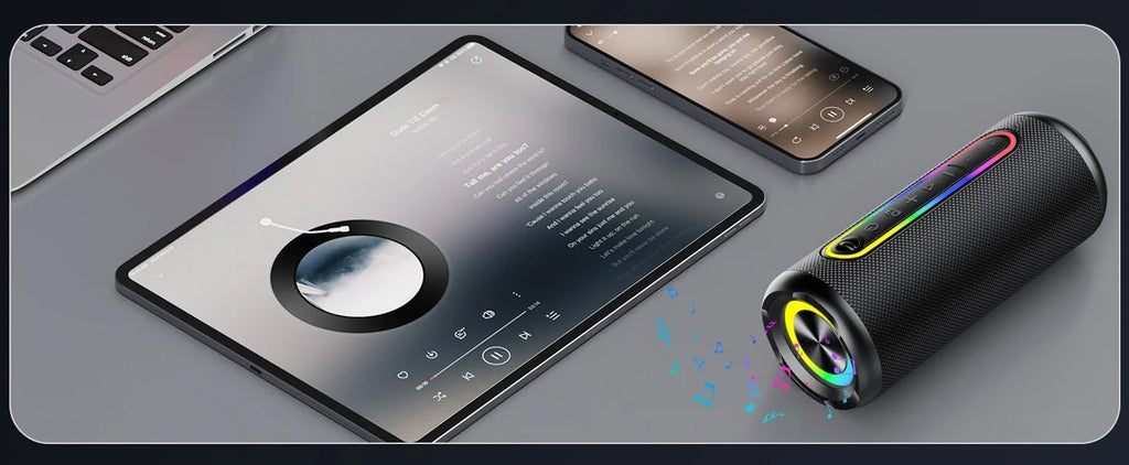 Black cylindrical portable Bluetooth speaker with vibrant LED light ring and music controls on a desk with devices.