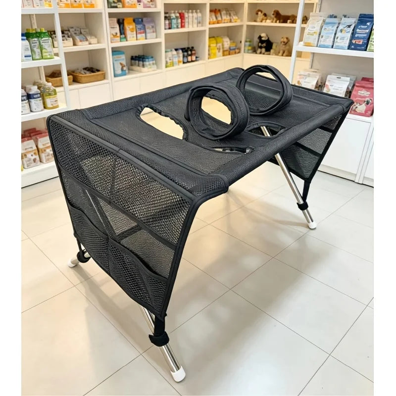 Black pet grooming hammock with metal legs, mesh pockets, and two leg support loops on top.