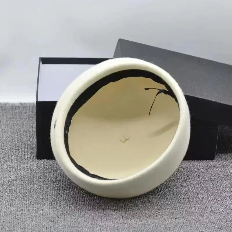 Interior view of a classic cream-coloured wool felt women's beret with a black lining, resting in an open gift box.