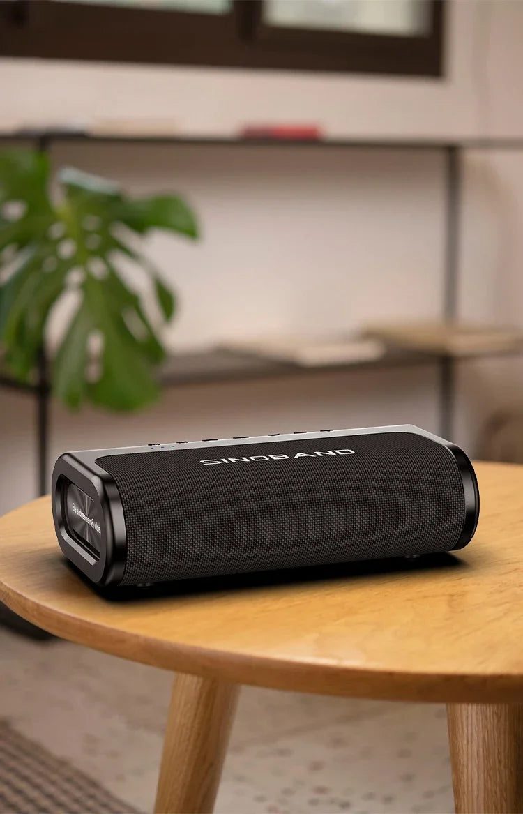 A sleek, black 80W wireless portable Bluetooth speaker with mesh fabric finish, sitting on a wooden table.
