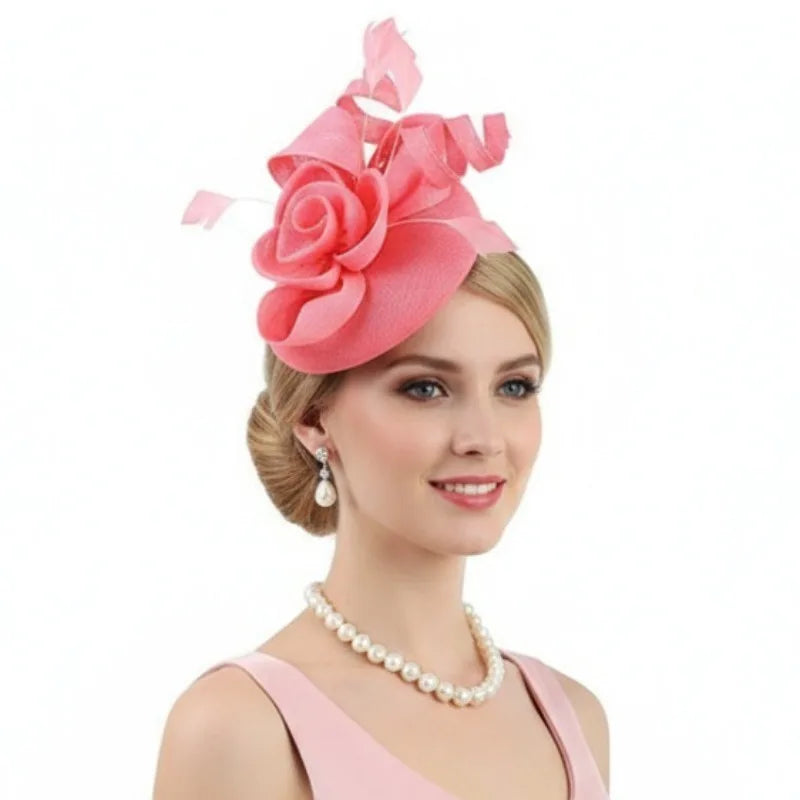 A woman wearing a vibrant coral-pink fascinator hat with a large fabric rose, sculptural ribbons, and delicate feathers.