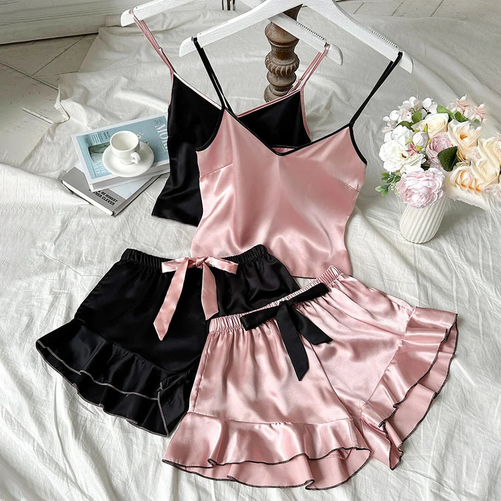 Two satin pyjama sets in black and pink, featuring camisole tops and ruffled shorts with delicate ribbon tie details.