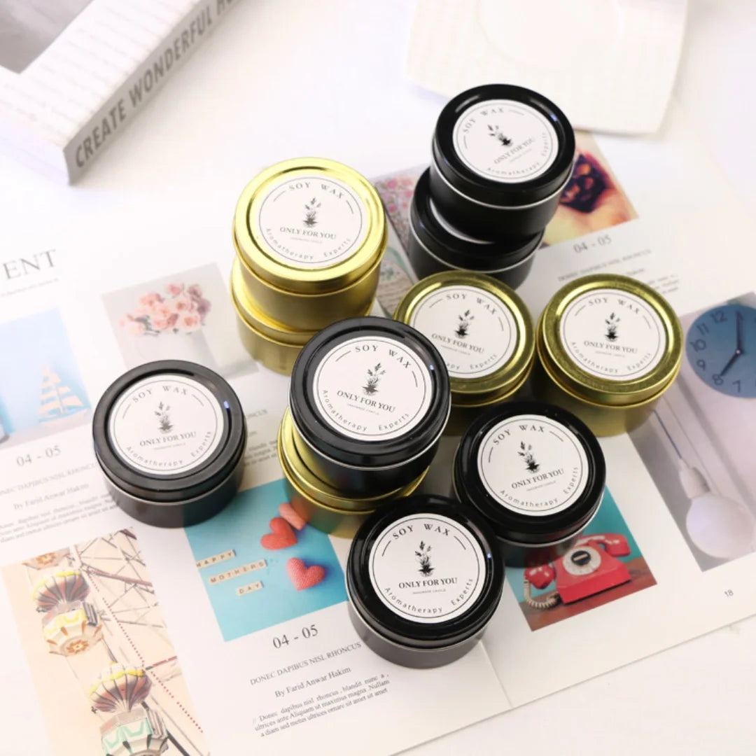 A collection of small, round soy wax aromatherapy candle tins in black and gold finishes with white labels.