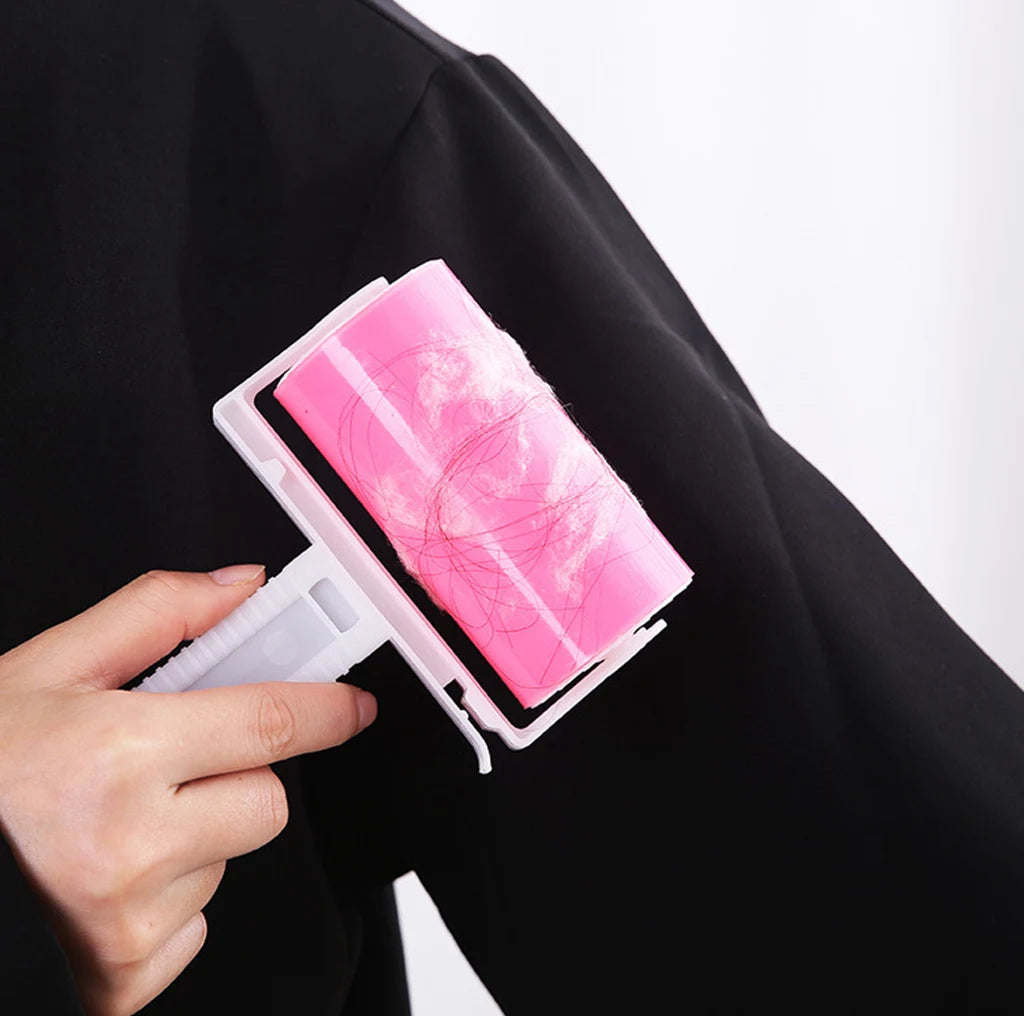 A hand uses a pink adhesive lint roller to remove hair and fluff from a black garment.