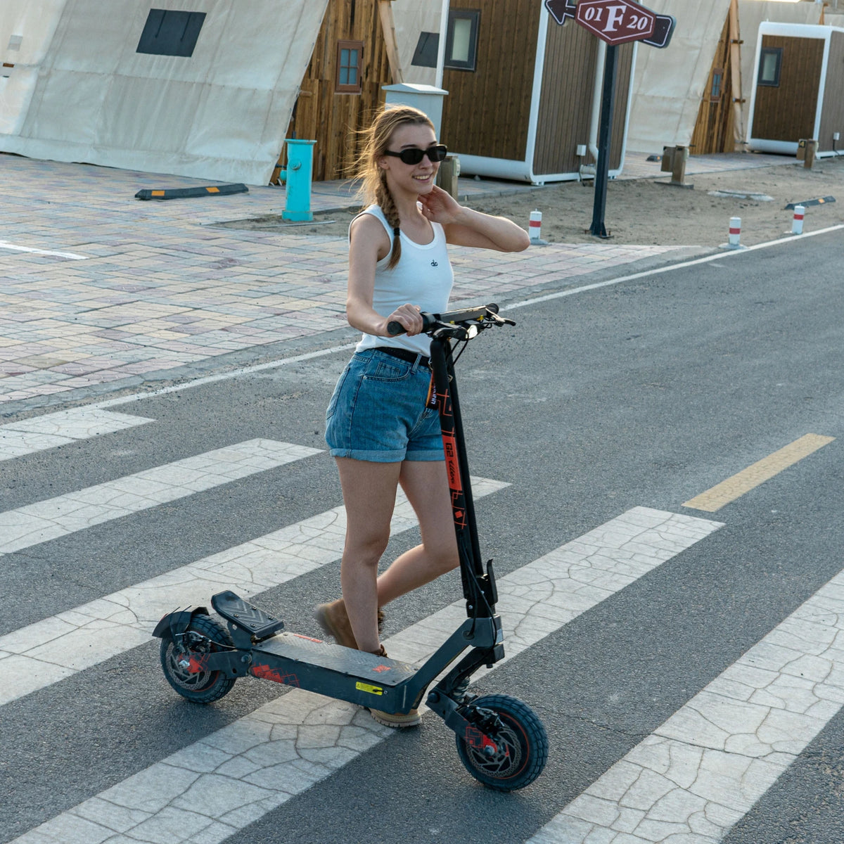 Woman riding a black KuKirin G2 Ultra electric scooter with orange accents, 10-inch tires, and dual brakes on asphalt.