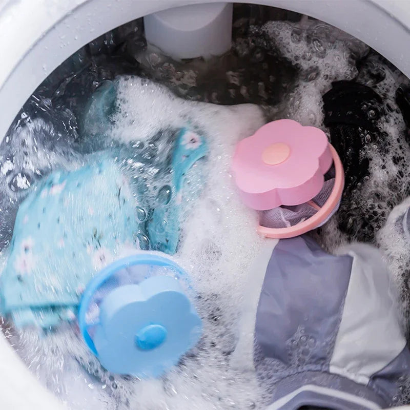 Pink and blue flower-shaped washing machine hair catcher mesh bags floating in soapy water with laundry.
