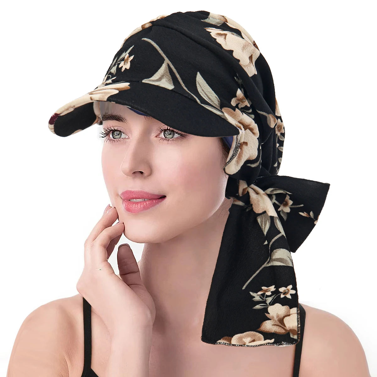 A woman wearing a vintage-style black turban hat with a beige floral pattern, a structured brim, and a side tie.