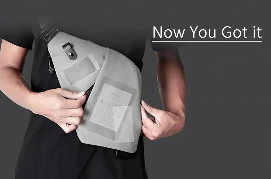 A grey, slimline anti-theft crossbody sling bag worn across the chest, showing compartments for a phone and e-reader.