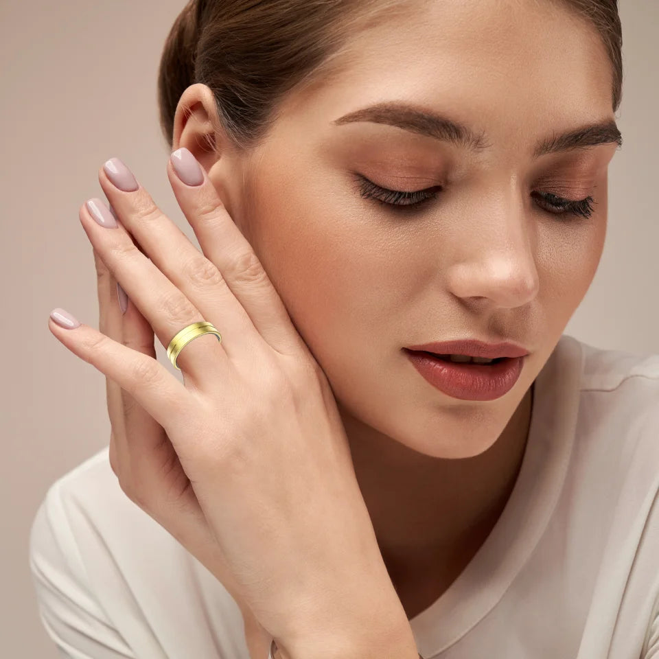 A woman wearing a sleek, polished gold smart fitness ring on her finger against a neutral background.