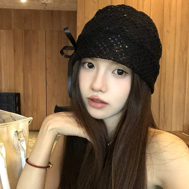Elegant black knitted hat with a delicate bow detail and subtle sparkle, worn by a woman with long dark hair.
