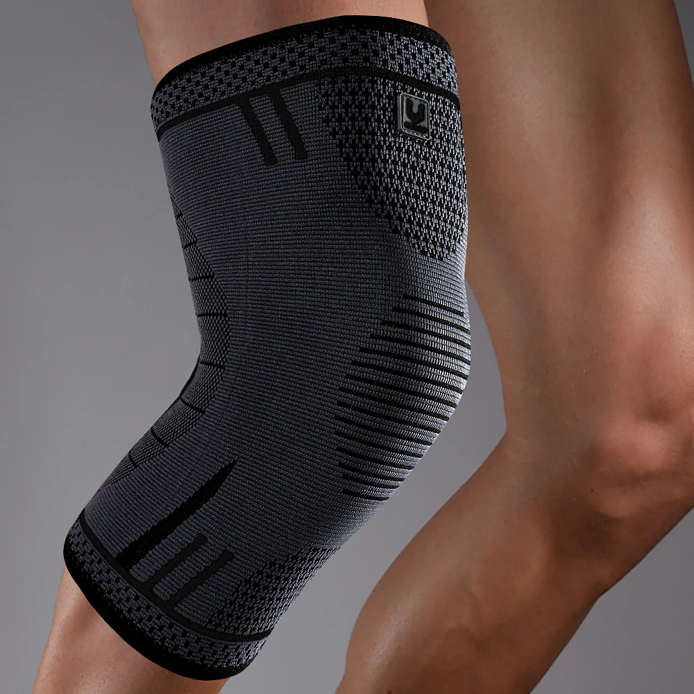 A grey and black compression knee support sleeve with targeted knit patterns worn on a person's leg.